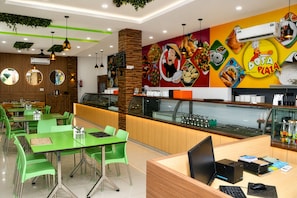 Un restaurante con mesas y sillas verdes, una barra con una computadora y una pared decorada con ilustraciones de comida.