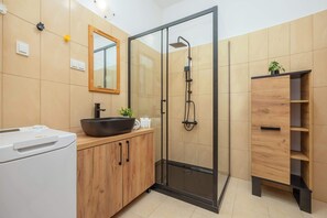 Un baño moderno con ducha envuelta en vidrio, tocador de madera y lavamanos de cuenca grande.