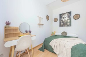 Makuuhuone, jossa on sänky, työpöytä tuolilla, peili, seinätaidetta ja makramee-seinävaate.