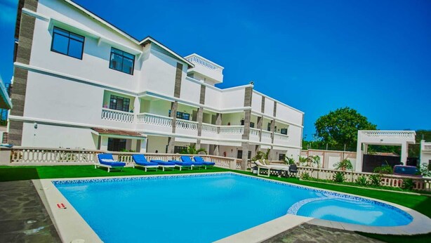 Un hotel de varios pisos con piscina, asientos exteriores y una zona cubierta.