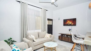 Una sala de estar con sofá, mesa de centro, televisor y comedor con sillas.