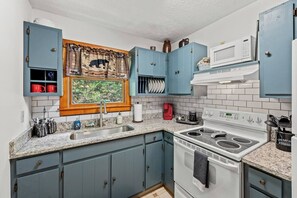 Eine Küche mit blauen Schränken, einem weißen Herd und einem Fenster mit Vorhang.