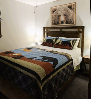 Ein Bett mit Decke, einem Kopfteil, einem Wandbild und einem Nachttisch mit Lampe.