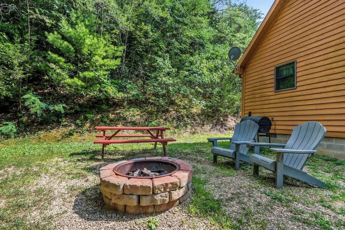 Une cabane en bois avec un foyer et des fauteuils Adirondack dans la cour.