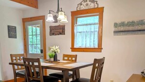 Un'area pranzo con un tavolo e sedie in legno, un tappeto, una finestra con tende e un cartello appeso al muro.