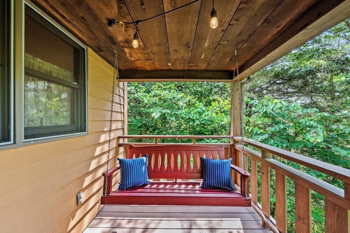 Une véranda en bois avec un banc rouge et des coussins bleus, donnant sur un paysage verdoyant et luxuriant.