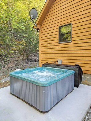 Ein Whirlpool vor einer Holzhütte mit Satellitenschüssel und kleinem Fenster.