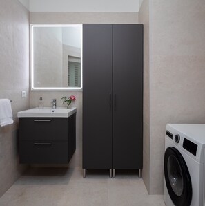Een moderne badkamer met een wastafel, spiegel, donkere kastjes en een wasmachine.