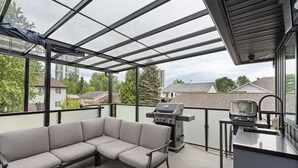 A covered outdoor area with a grill, a sofa, and a countertop. - Modern 5BR Home Near Lions Gate | Glass Deck + BBQ (West Vancouver)