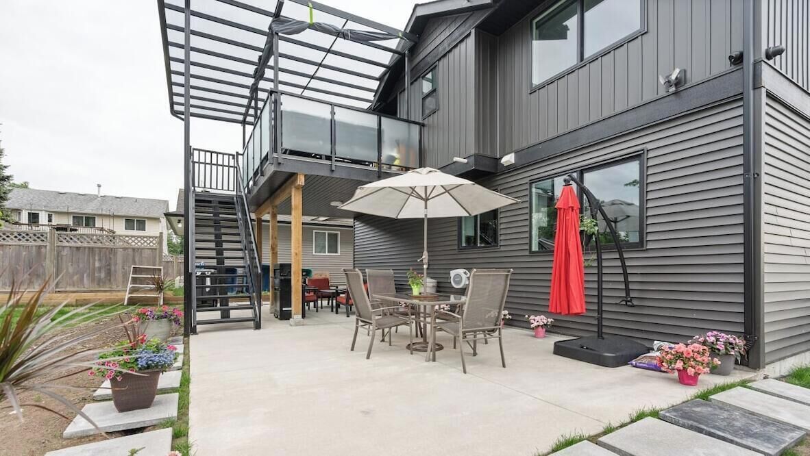 Una casa moderna con un patio, mobiliario exterior y una zona cubierta.