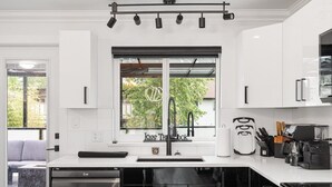 A modern kitchen with a large window, a built-in dishwasher, and a coffee machine. - Modern 5BR Home Near Lions Gate | Glass Deck + BBQ (West Vancouver)