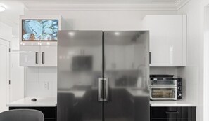 Eine moderne Küche mit einem Edelstahl-Kühlschrank, einem eingebauten Backofen und einem flachbildfernseher, der über dem Kühlschrank angebracht ist.
