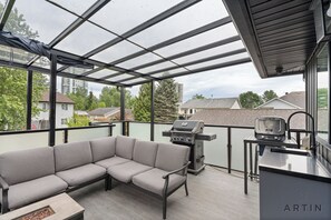 Un balcon abrité équipé d’un barbecue, d’un canapé et d’une petite table.