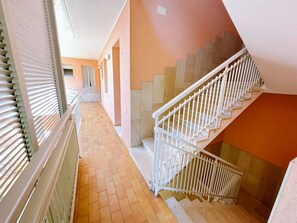 Ein Korridor mit gefliestem Boden, einer Treppe mit weißen Geländern und einer Tür in der Wand.