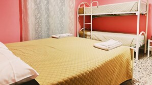 Ein Zimmer mit einem Etagenbett, einem Einzelbett, einem Fenster mit leichtem Vorhang und einem gemusterten Boden.