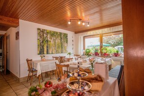 Zona pranzo con tavoli e sedie di legno, un quadro grande appeso al muro e vista dalla finestra.