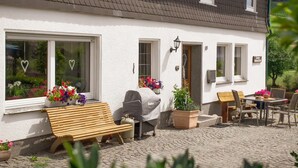 A white building with a tiled roof, a wooden bench, a barbecue grill, and outdoor seating. - Wiebelhaus-Mester Farm Guesthouse – Schwalbennest Holiday Apartment (Lennestadt)