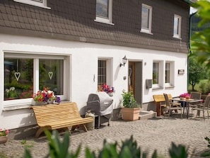 Ein weißes Gebäude mit Ziegeldach, einer Holzbank, einem Grill und Außenmöbeln.