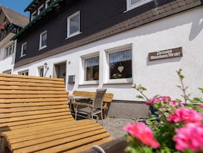 Ein traditionelles Gebäude mit einem Schild, das 'Pension Dietelhaus Meister' zeigt, Sitzgelegenheiten im Freien und einem steinernen Weg.