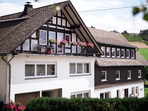 Ein zweistöckiges Haus mit Balkon, großen Fenstern und einem geneigten Dach.