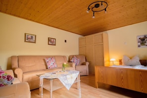 A cozy living room with a wooden ceiling, a sofa, a coffee table, and a bed with a wooden headboard.