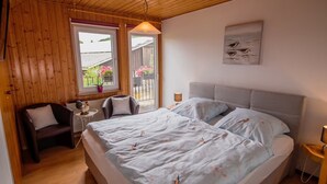 Een slaapkamer met een bed, een stoel, een klein tafeltje, een lamp en een raam met uitzicht.