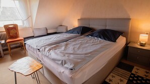 A bedroom with a bed, bedside table, chair, and a radiator.