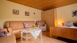 A cozy living room with a wooden ceiling, a sofa, a table with a tablecloth, and a bed with a wooden headboard.