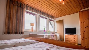 A bedroom with two beds, a wooden ceiling, a TV, and a window with curtains.