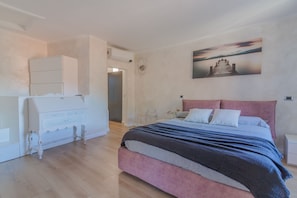 A bedroom with a bed, a dresser, a painting on the wall, and a door leading to another room.