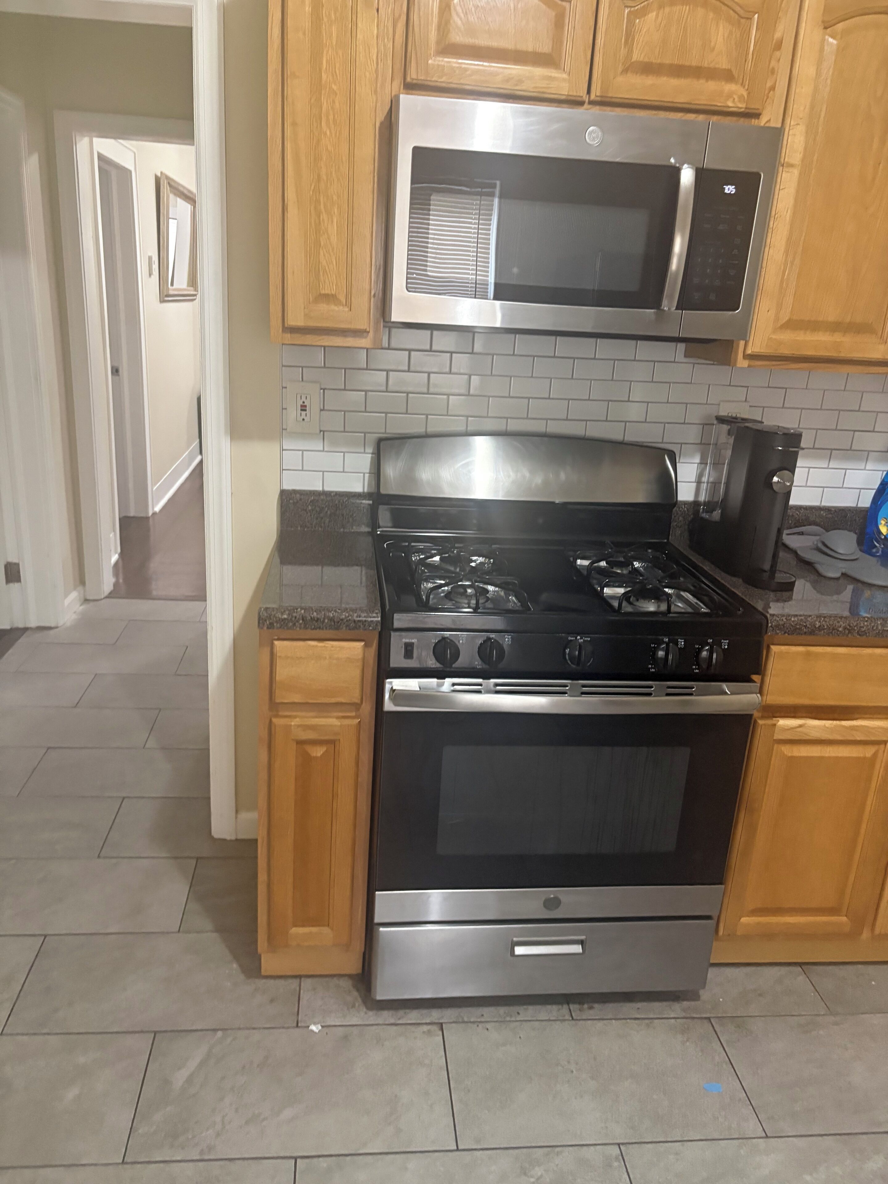 Una cucina con piano cottura in acciaio inossidabile, forno a microonde, mobili in legno e zoccolo paraschizzi rivestito di piastrelle.