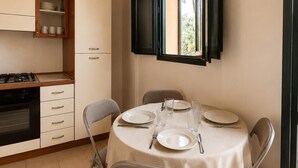 A compact kitchen with a dining area, a window with blinds, and a view of greenery outside. - Ulysse77 - Ocean-View House with Pool & Garden (syvota)