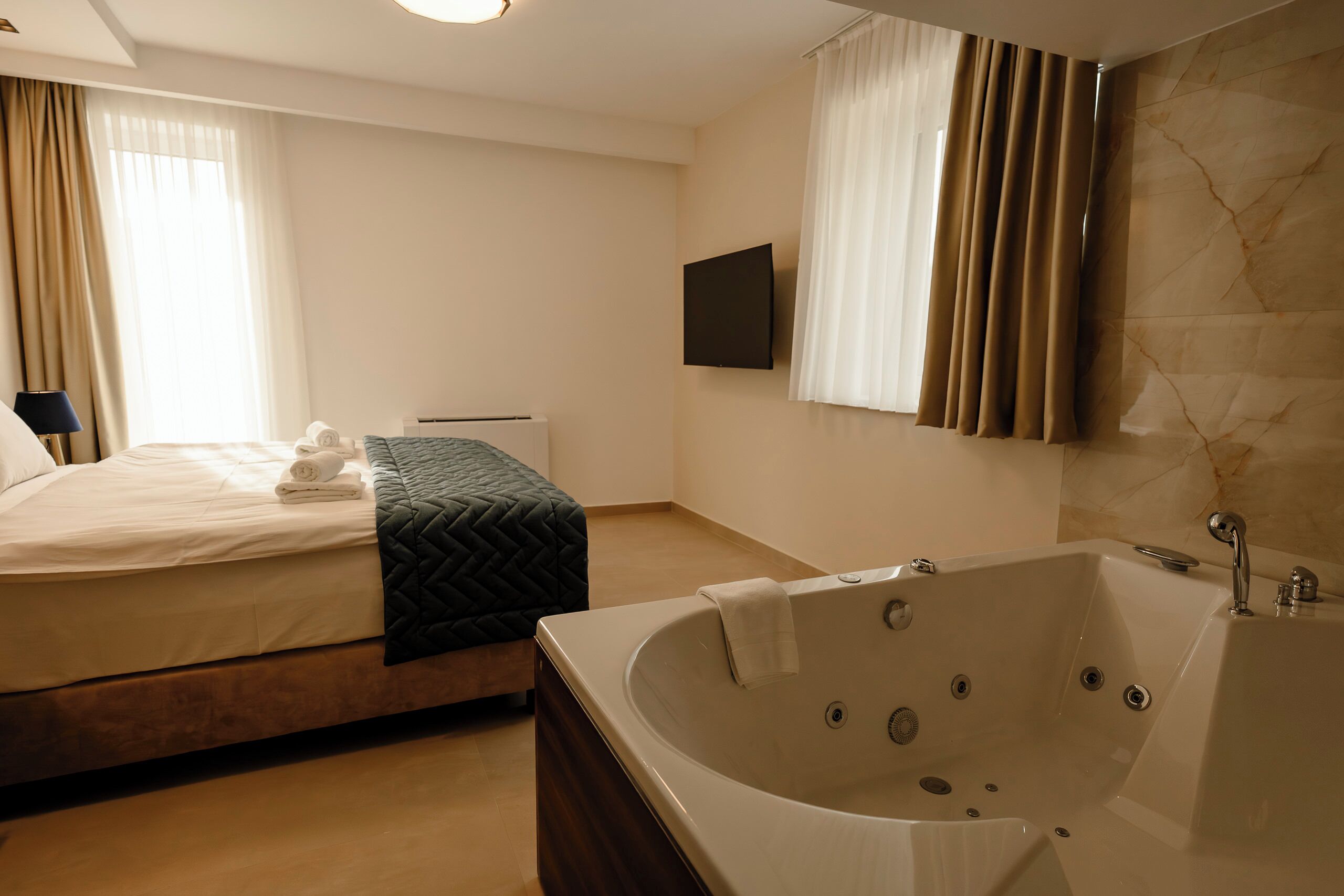 Habitación de hotel con cama, una bañera grande, televisor de pantalla plana y pared de mármol.