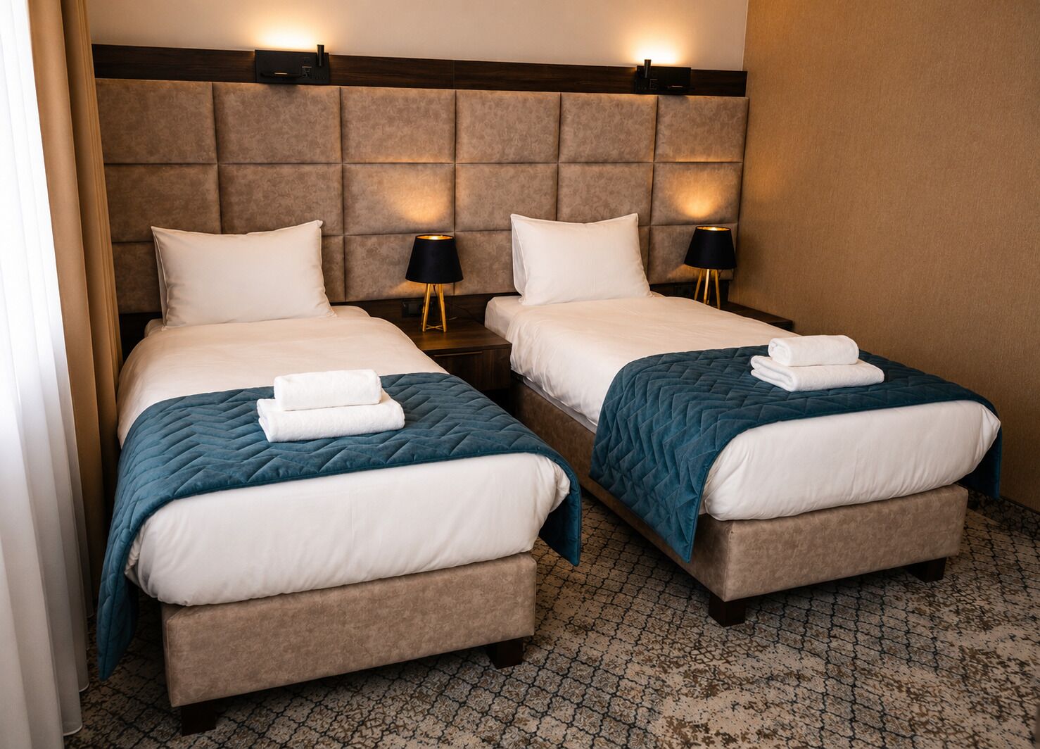 Camera d'albergo con due letti, ciascuno con un cuscino, un comodino con una lampada e una coperta trapuntata.