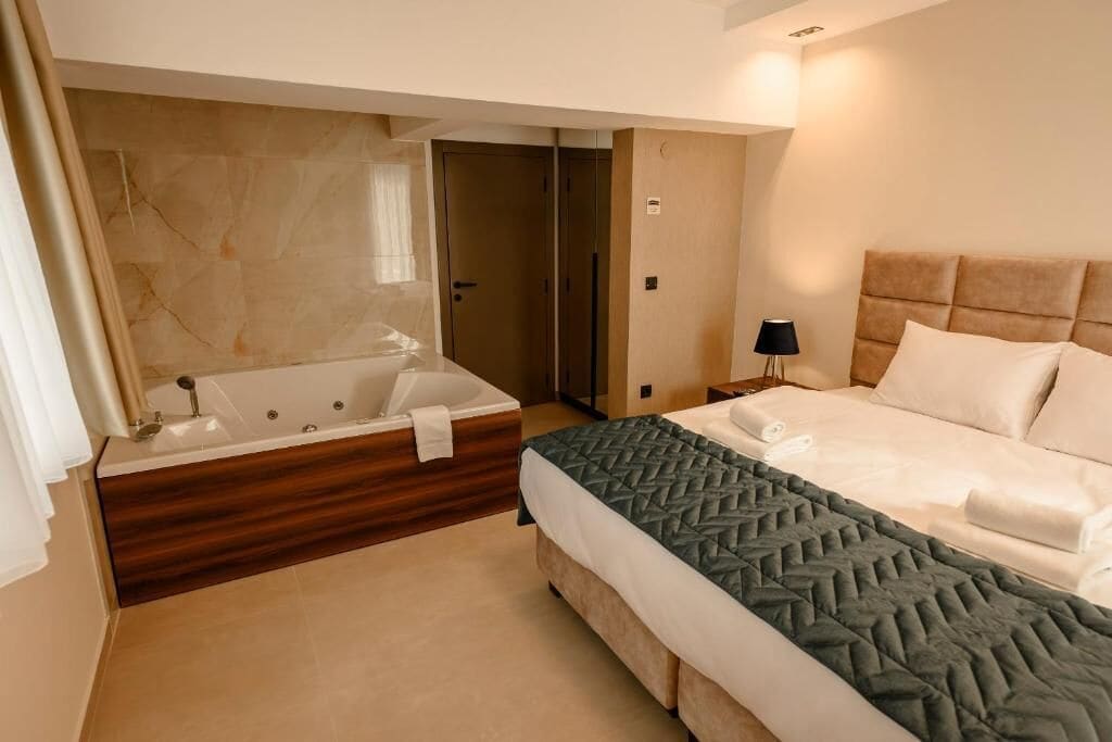 A hotel room with a large bathtub, a bed with a quilted bedspread, and a nightstand with a lamp.