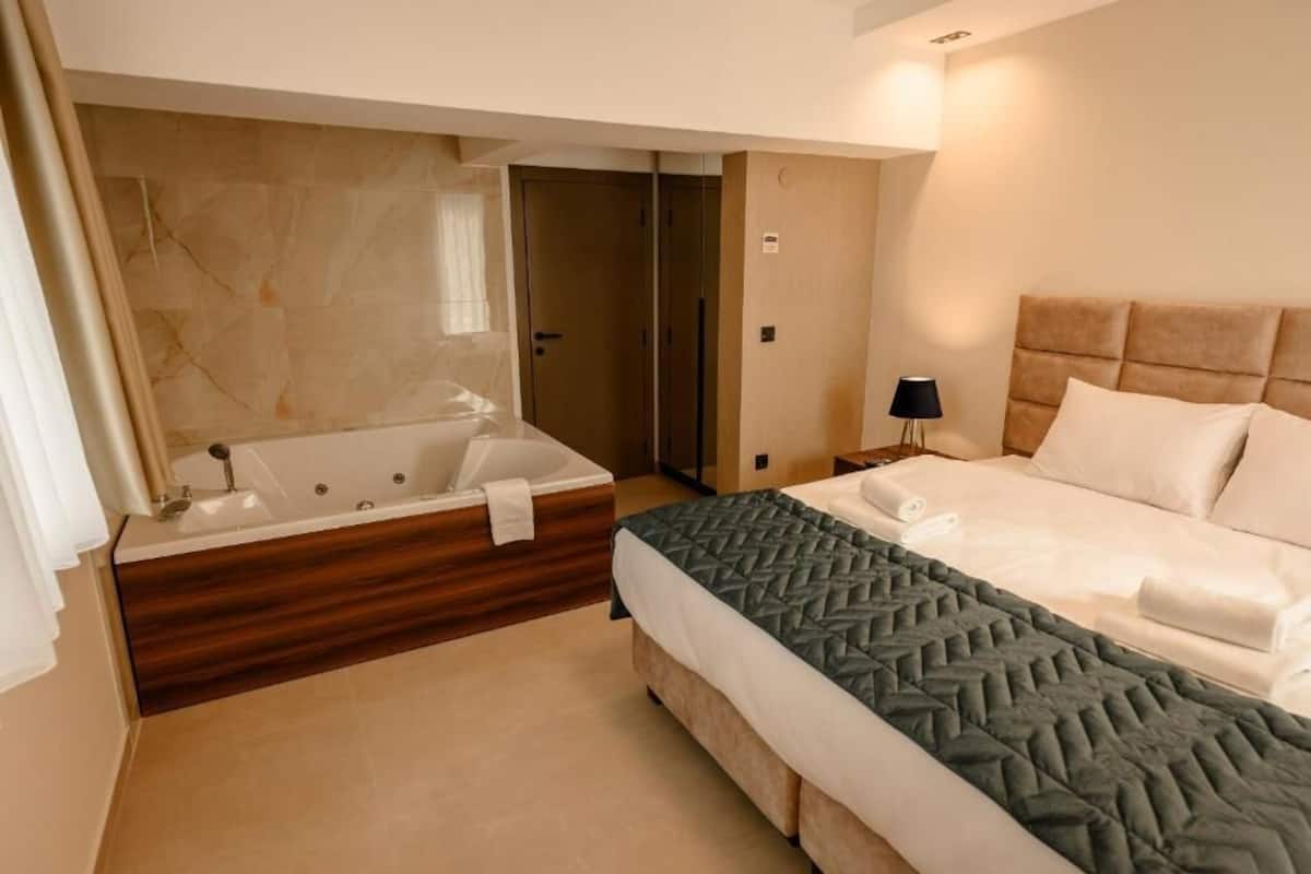 Una habitación de hotel con una bañera grande, una cama con colcha acolchada y una mesita de noche con lámpara.