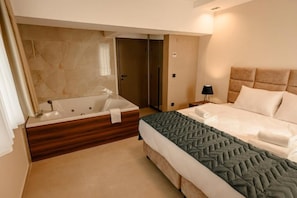 Una habitación de hotel con una bañera grande, una cama con colcha acolchada y una mesita de noche con lámpara.