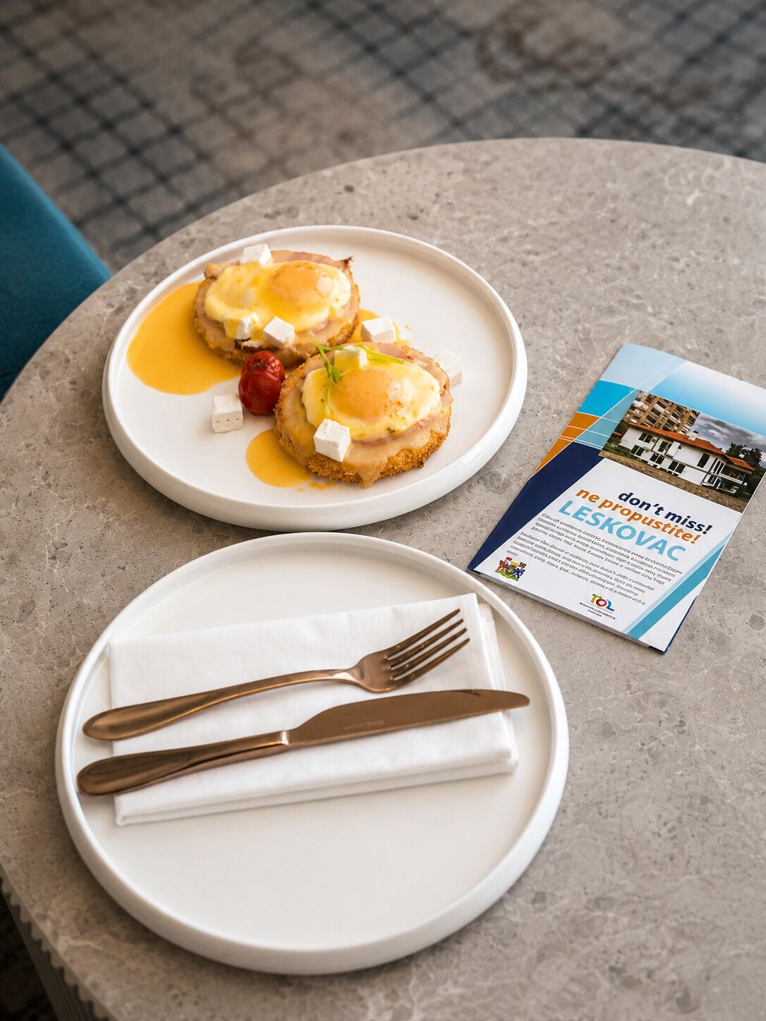Two plates of food on a table with a brochure and cutlery.