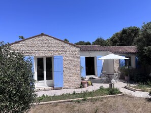 Ein Haus aus Stein mit blauen Fensterläden, einer Terrasse mit Gartenmöbeln und einem Garten.