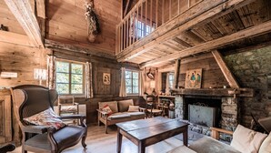 Interior rústico de una cabaña con pisos de madera, chimenea, comedor y un altillo.