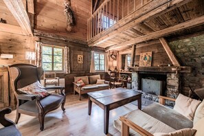 A rustic cabin interior with wooden floors, a fireplace, a dining area, and a loft space.