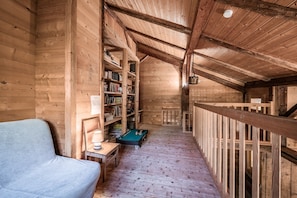 A wooden interior with a sofa, bookshelves, a pool table, and a wooden railing.