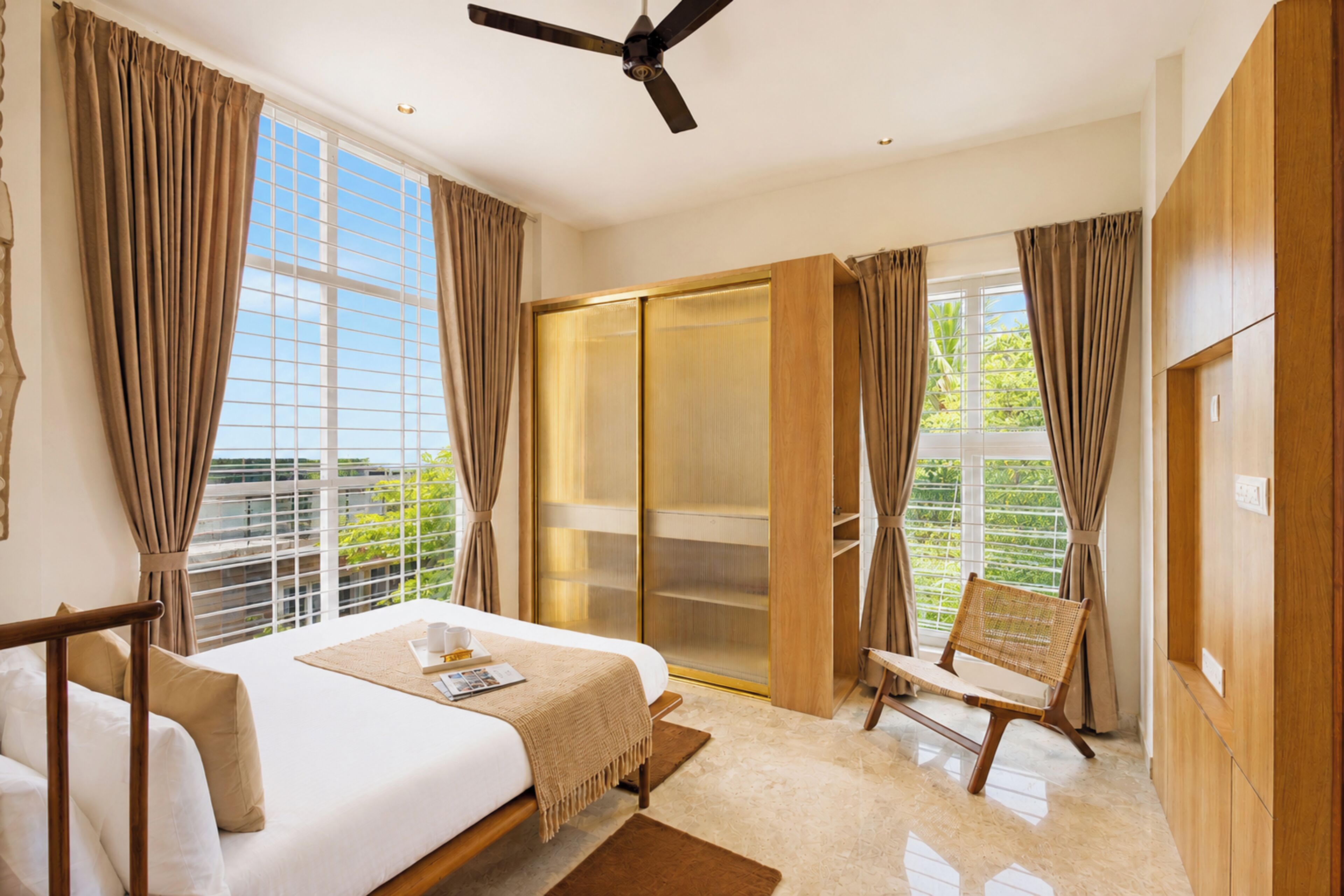 A bedroom with a bed, a chair, a ceiling fan, and a sliding glass door leading to a balcony.