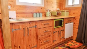 A compact kitchen with wooden cabinets, a microwave, a toaster, and a small refrigerator. - The Cabin (Amlwch)