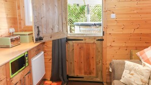 A compact kitchen with wooden walls, a window with a view, a microwave, a toaster, and a small refrigerator. - The Cabin (Amlwch)