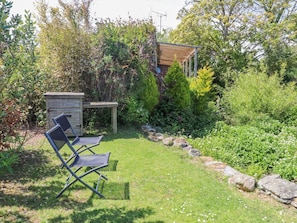 A garden with a wooden structure, a metal chair, and a small shed. - The Cabin (Amlwch)