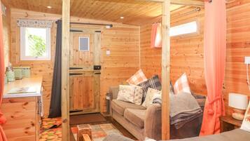 A wooden cabin interior with a kitchenette, a sofa, and a bed.