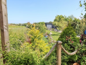 A garden with a wooden fence, a rope gate, and a building in the background. - The Cabin (Amlwch)