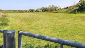 A grassy field with a metal fence in the foreground. - The Cabin (Amlwch)