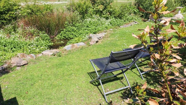 A grassy outdoor area with a metal chair and a stone pathway. - The Cabin (Amlwch)